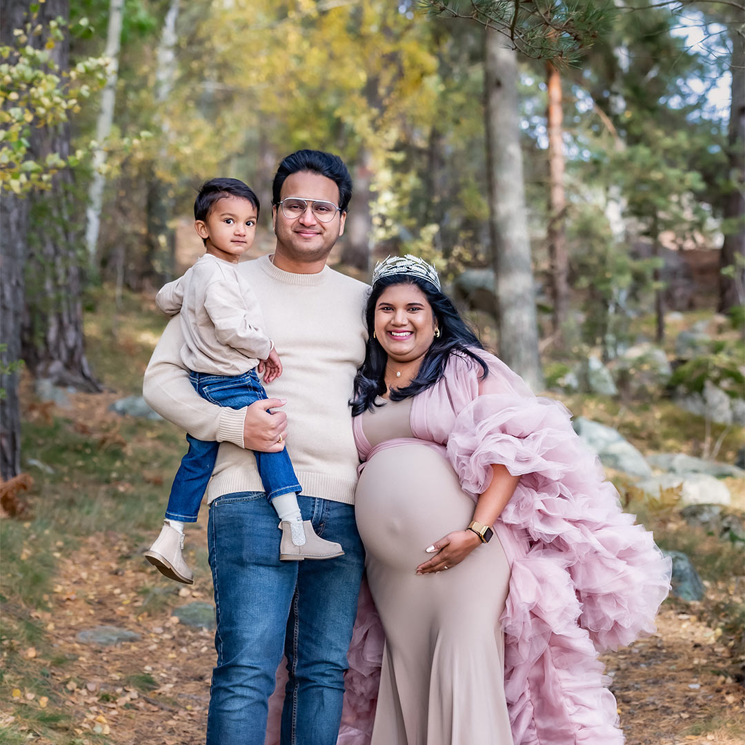 Gravidfotografering med en familj om hösten. De står på en stig i skogen.
