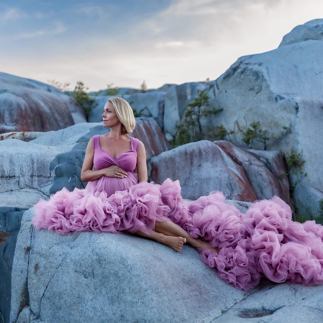 Gravidfotografering i ett kalkbrott. Den gravida kvinnan har på sig en lyxig rosa tyllklänning och sitter på en klippa.