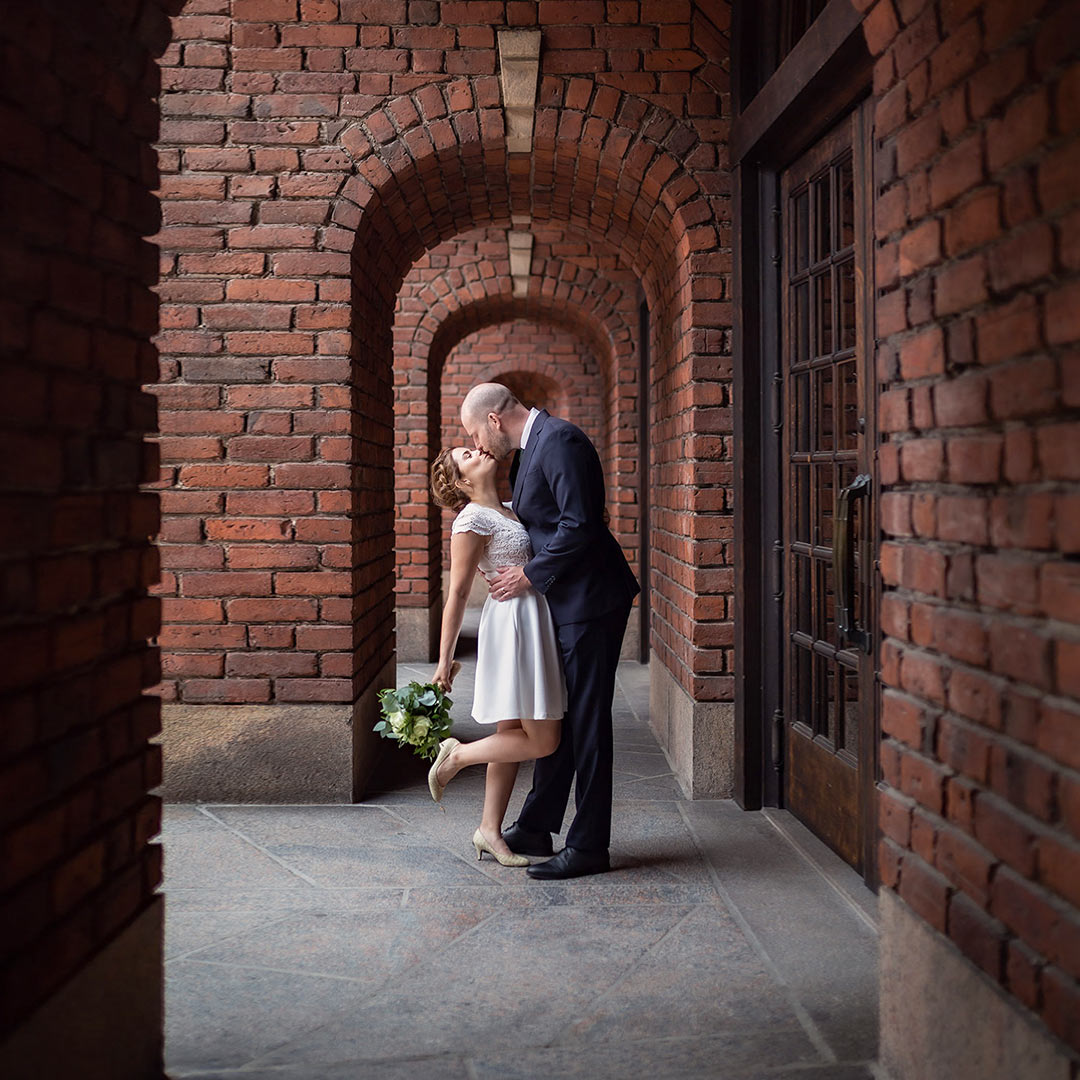 Brudpar pussas i en korridor i en gammal byggnad byggd av röda tegelstenar.