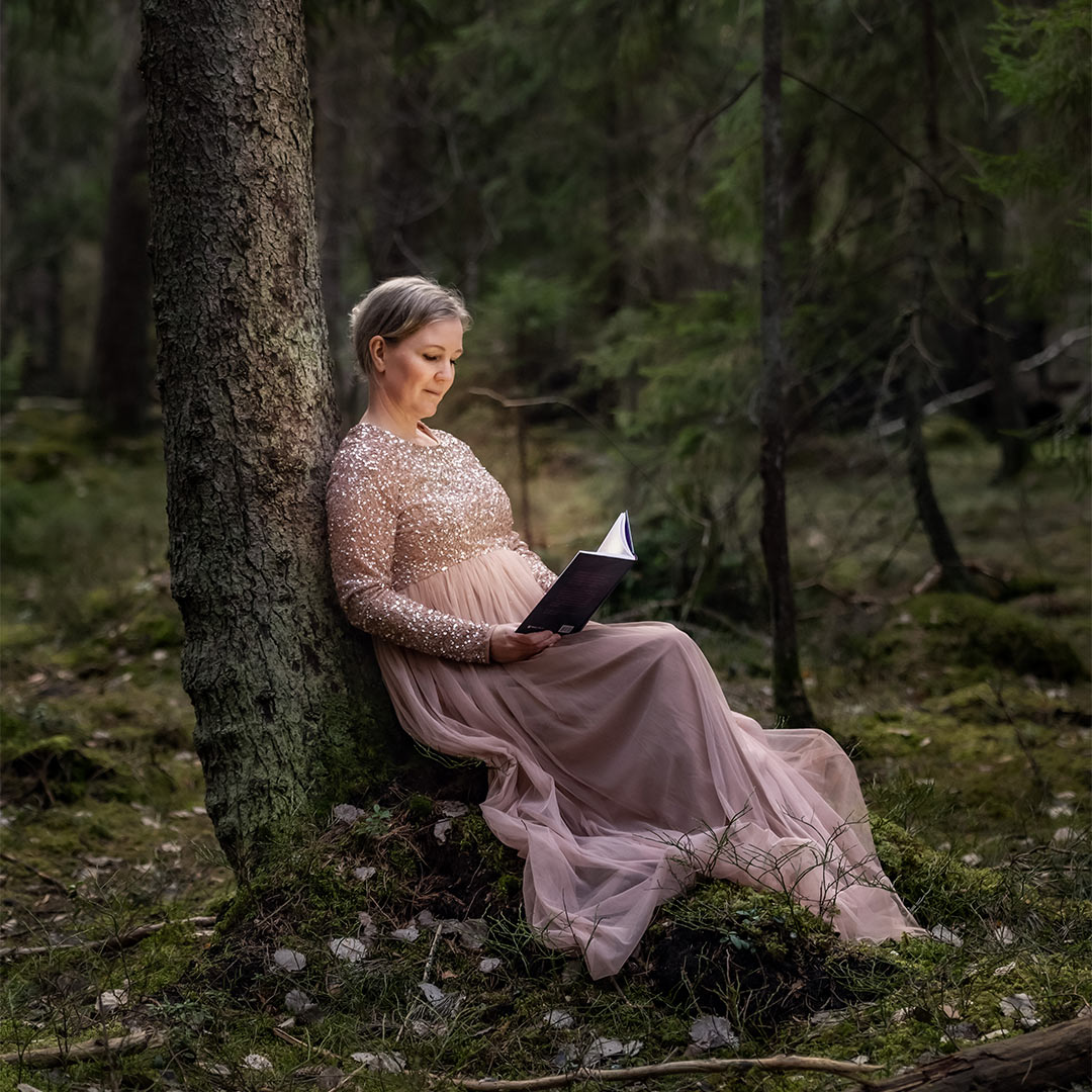 Fotografering av författaren Linda Wahlund. Linda Wahlund sitter mot ett träd och läser en bok. Från boken kommer ett magiskt sken som lyser upp Linda.
