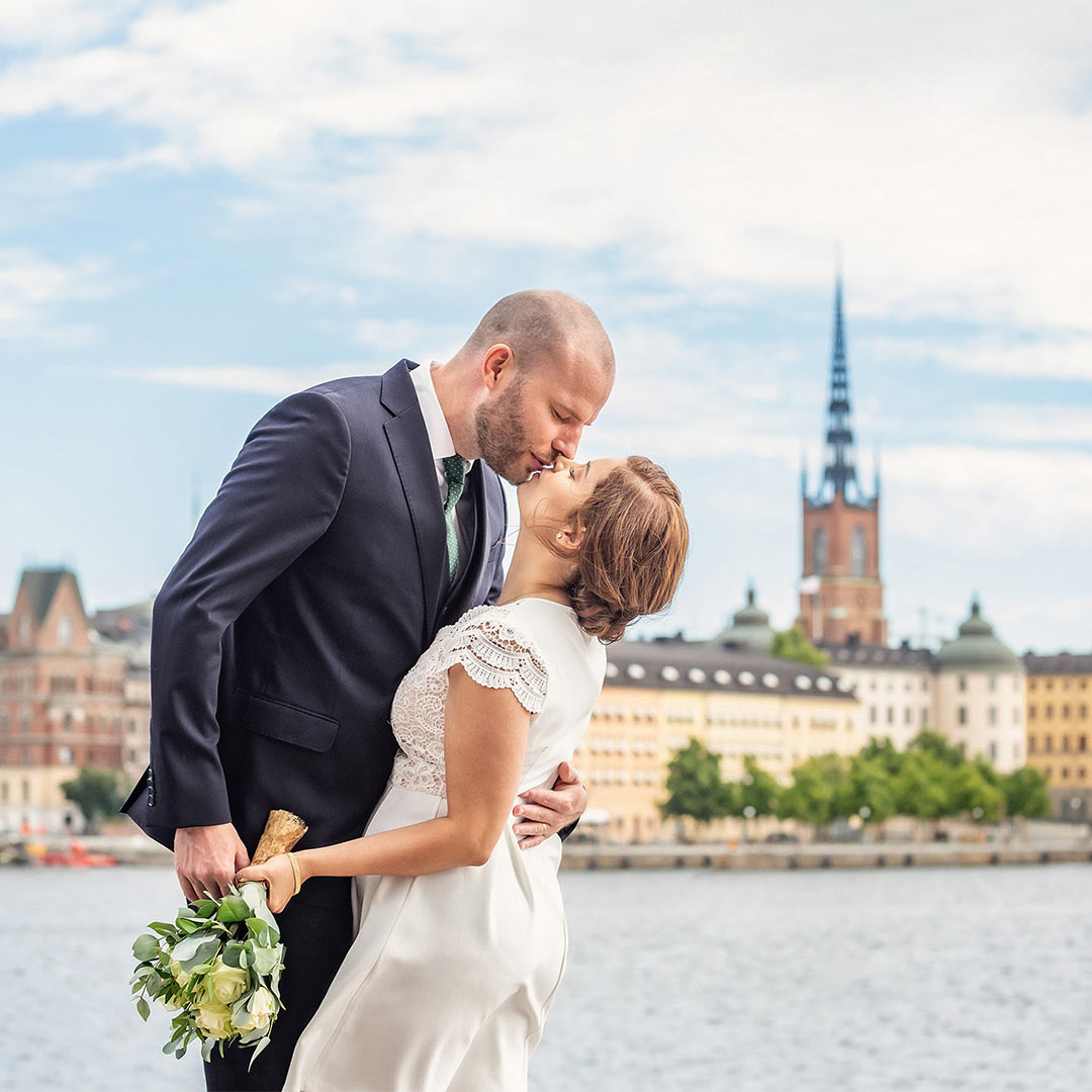 Ett brudpar pussas. I bakgrunden, på andra sidan vattnet, syns Gamla stan i Stockholm.