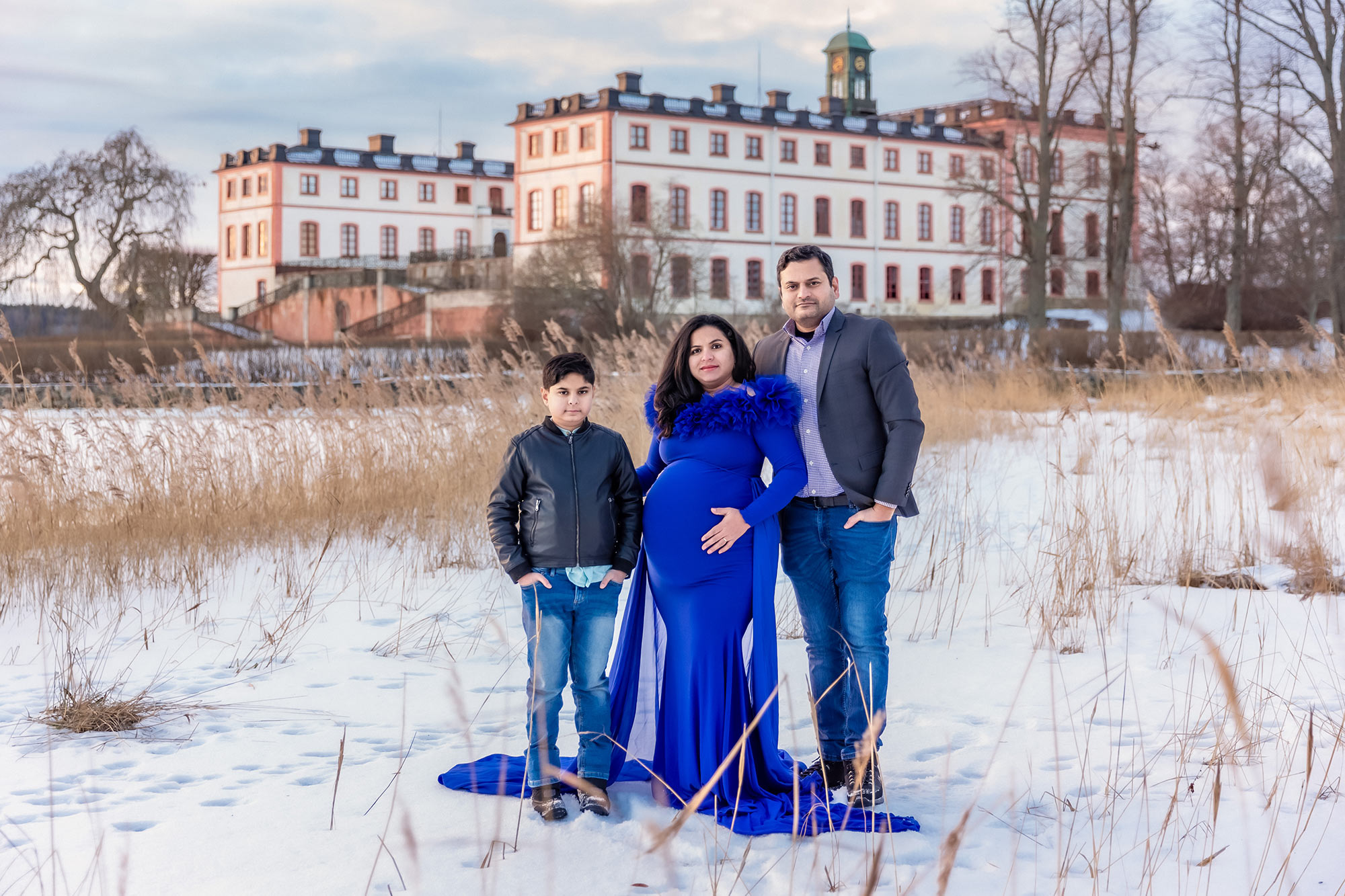 Gravidfotografering med familj framför Tullgarns Slott. Snön ligger tjock på marken och bakom familjen syns slottet.