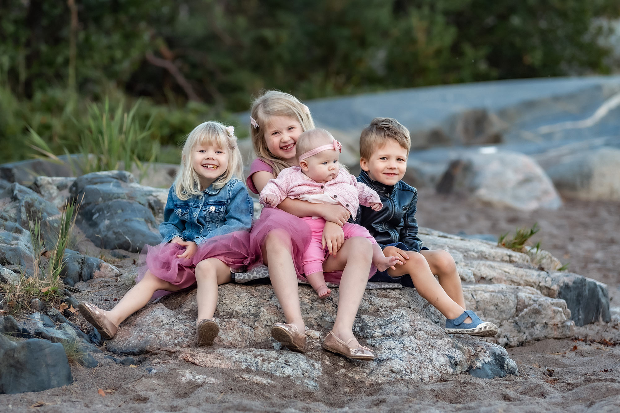 Fyra små syskon sitter på en sten och tittar in i kameran.