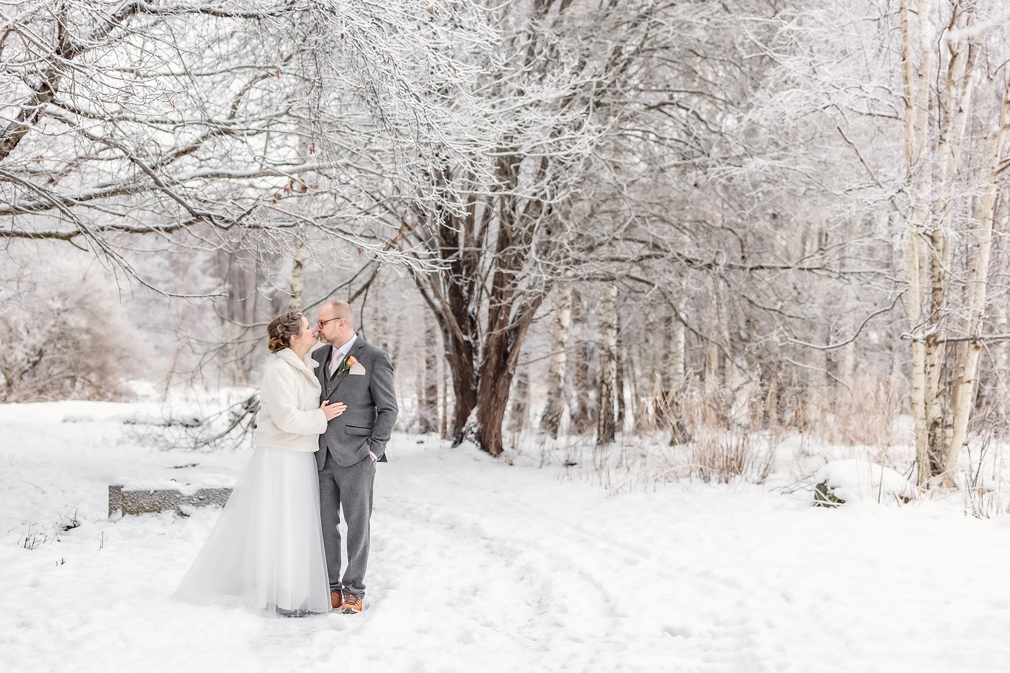 Bröllopspar står i ett snötäckt landskap där snön ligger tjock på trädgrenarna.