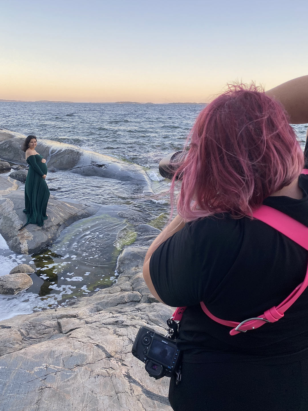 Gravidfotograf Linda Holmkratz fotograferar en gravid kvinna på klipporna vid havet. Bilden är tagen av den blivande pappan.