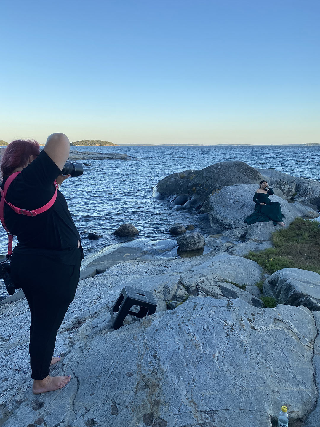Gravidfotograf Linda Holmkratz fotograferar en gravid kvinna på klipporna vid havet. Bilden är tagen av den blivande pappan.