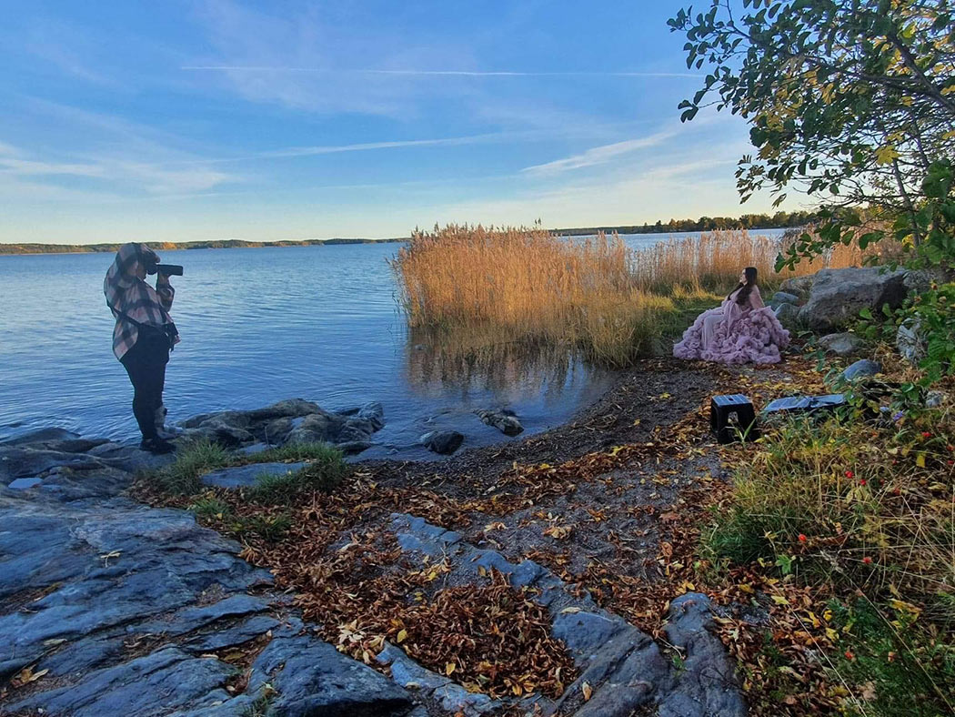 Gravidfotograf Linda Holmkratz fotograferar en gravid kvinna på en strand om hösten. Bland höstlöv, klippor och vacker vass. Bilden är tagen av den blivande pappan.