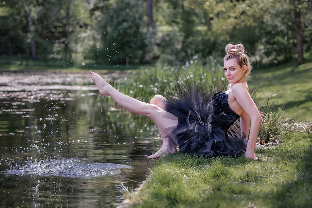 En kvinna i svart balettklänning skvätter med fötterna i vattnet.