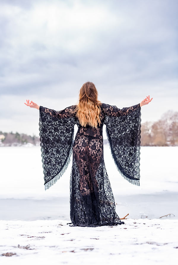 Kreativt porträtt med en kvinna i svart genomskinlig spetsklänning. Det är en kall vinterdag och världen är snötäckt.