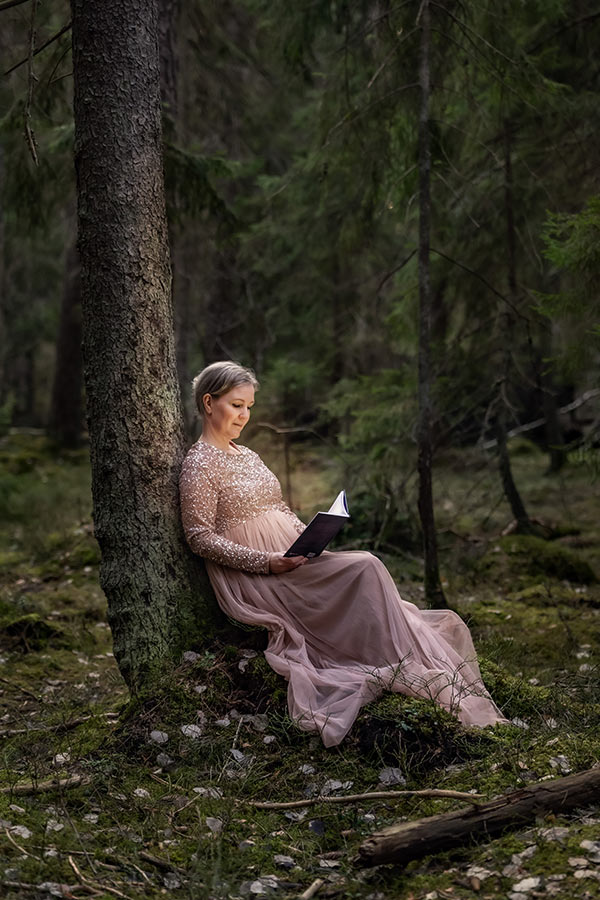 Kreativ fotografering med författaren Linda Wahlund, som sitter vi ett träd i skogen och läser sin egen bok som lyser upp henne.