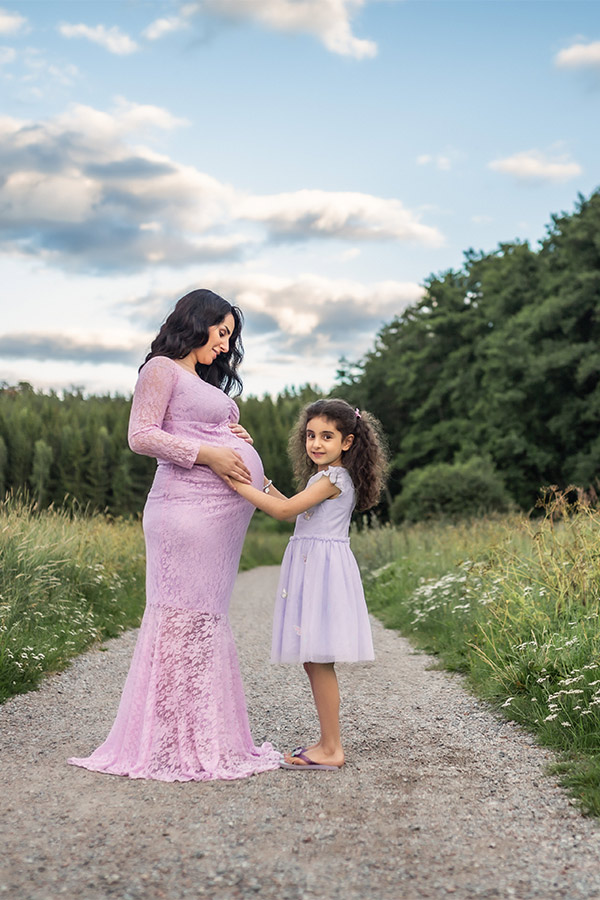 Fotografering med en gravid kvinna och hennes dotter på en stig genom en äng.