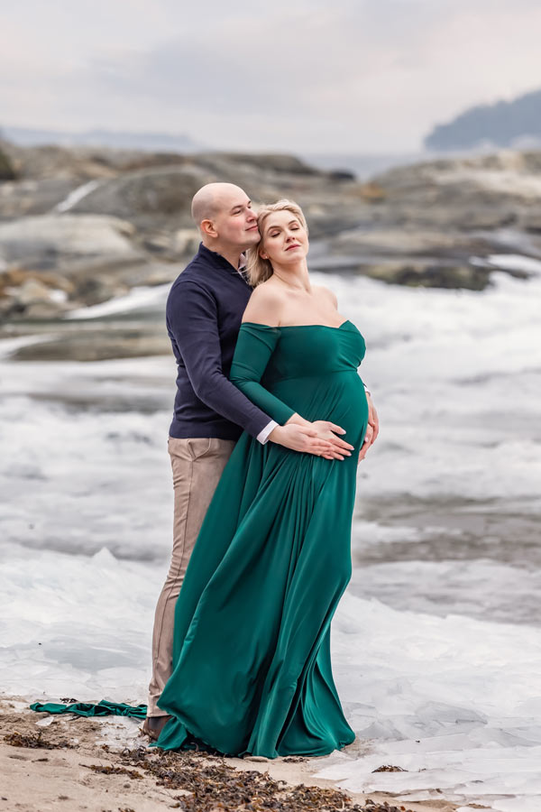 Ett vackert par står vid ett istäckt vinterhav. Kvinnan är gravid och har en grön klänning.