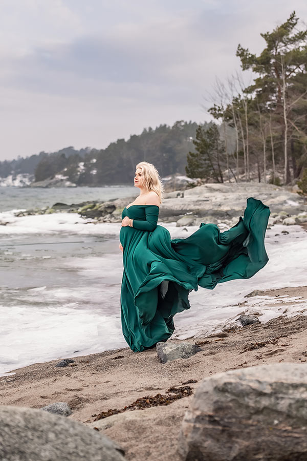 En gravid kvinna i grön flygande klänning står i stormen vid havet.