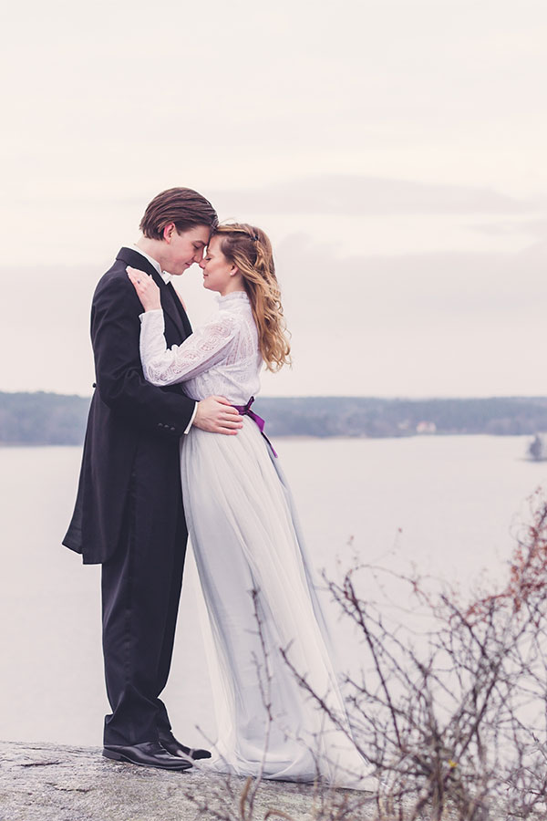 Kärlekspar pussas högt upp på en klippa med utsikt över ett vintrigt mälaren.