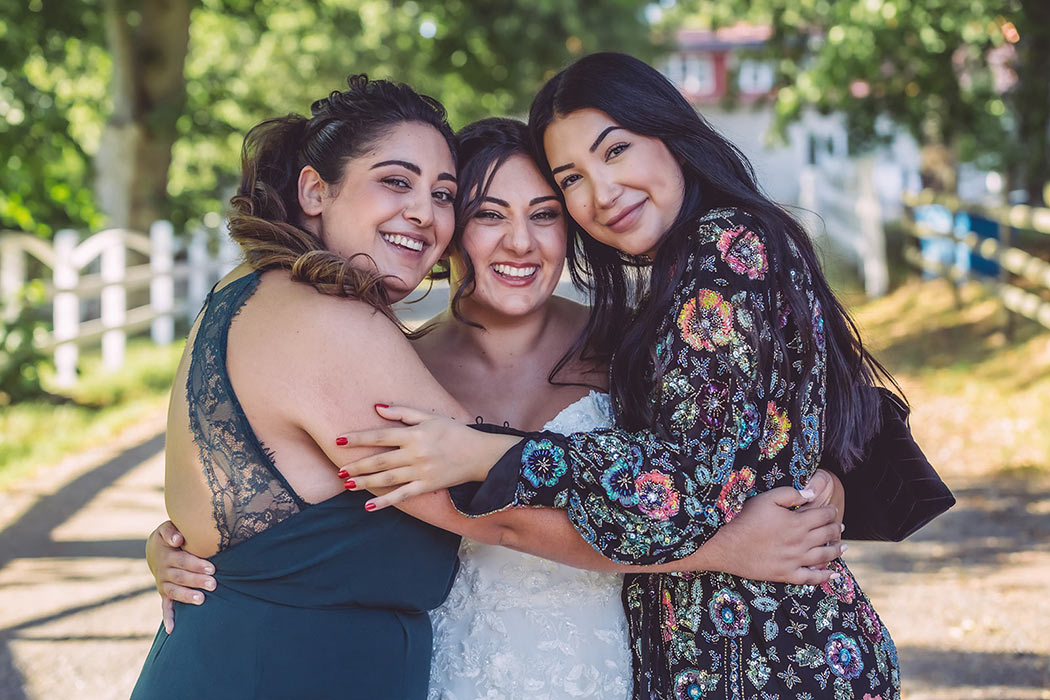 En nygift brud och hennes två vänner tittar in i bröllopsfotografens kamera och skrattar.