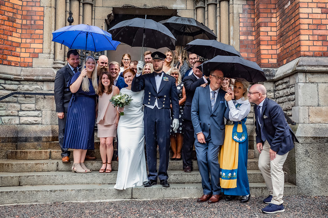 Brudpar och gäster står under paraplyer utanför kyrkan.