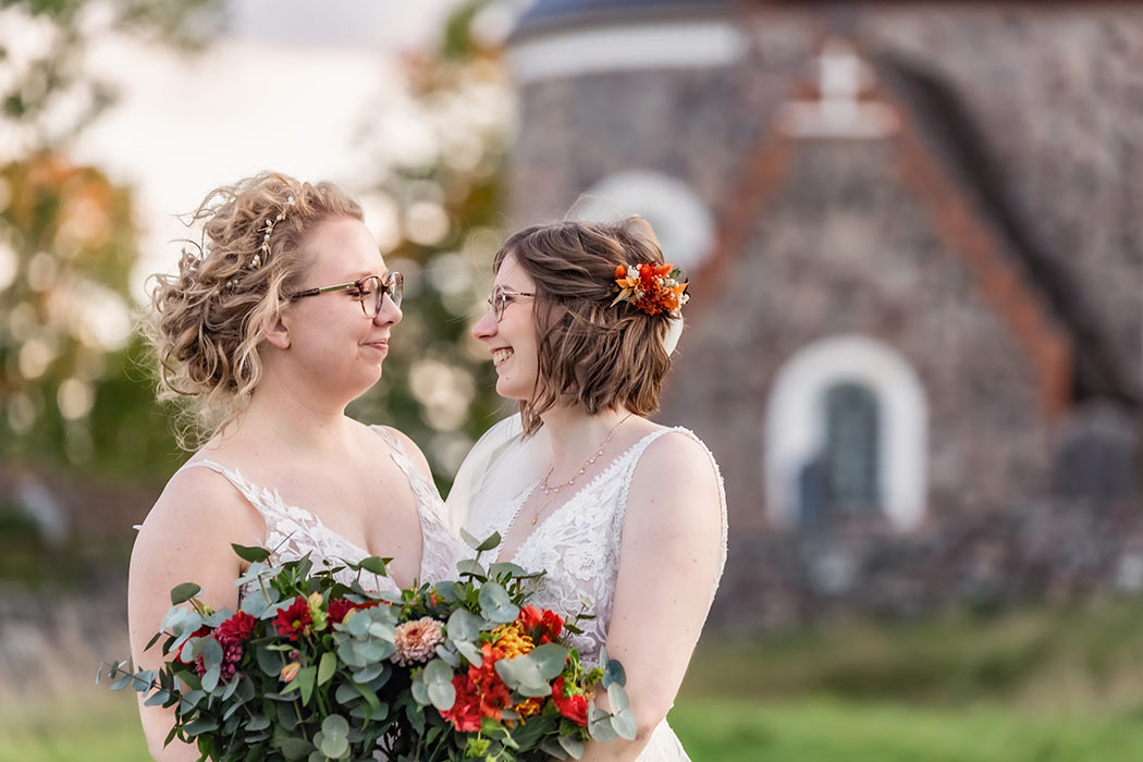 Brudparet tittar förälskat i ögonen på varandra framför Gamla Uppsala kyrka.
