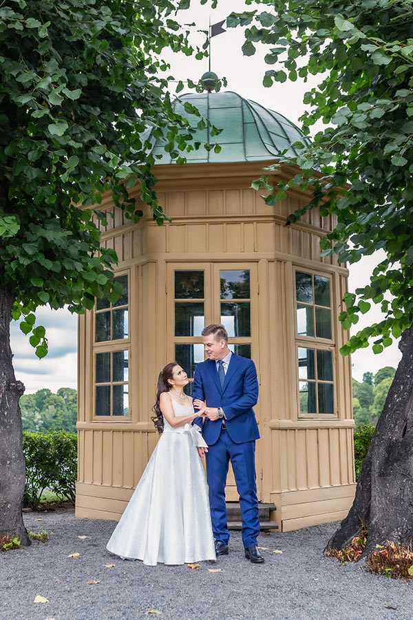 Ett brudpar står framför lusthuset vid Stallmästaregården och tittar på varandra.