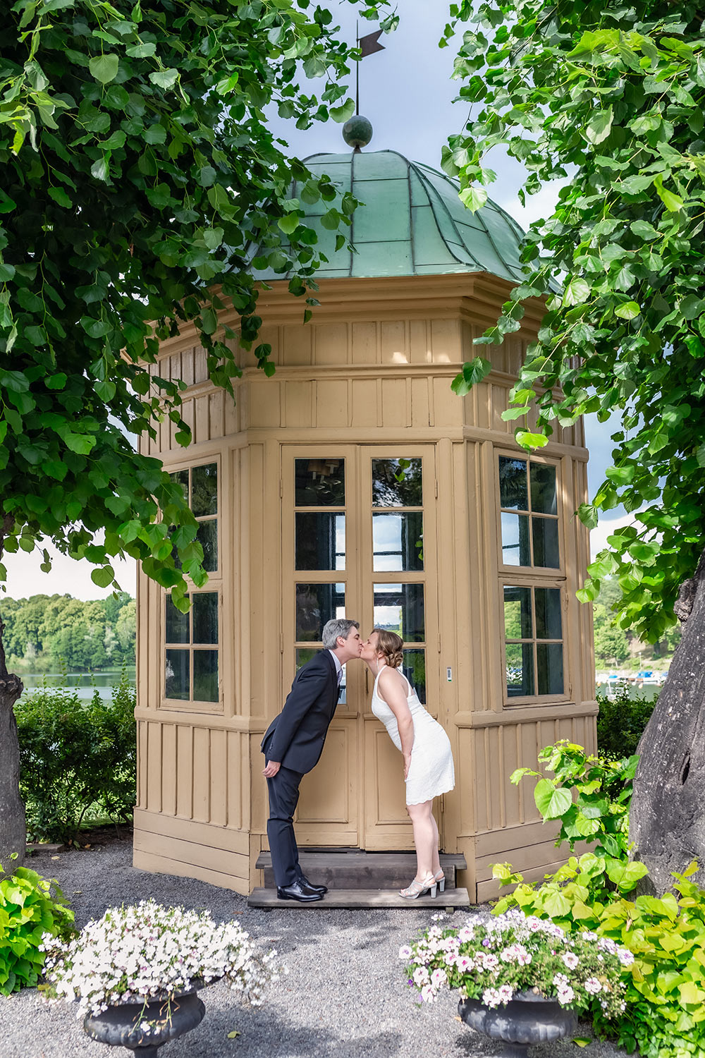 Bröllopspar pussar varandra på trappan till ett gult lusthus vid Stallmästaregården i Haga.