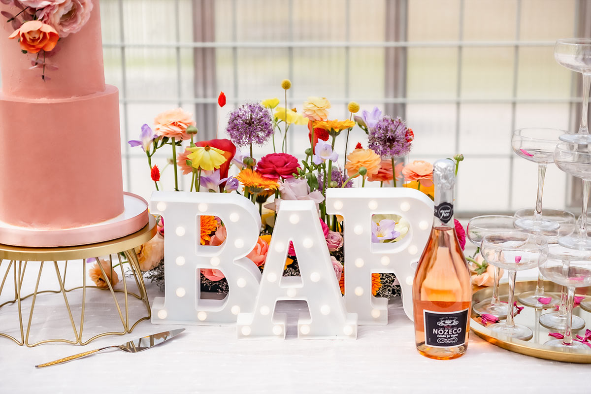 Ett vackert uppställt bord med tårta och bubbel. På bordet står en prunkande blomsterdekoration och stora bokstäver som bildar ordet BAR.