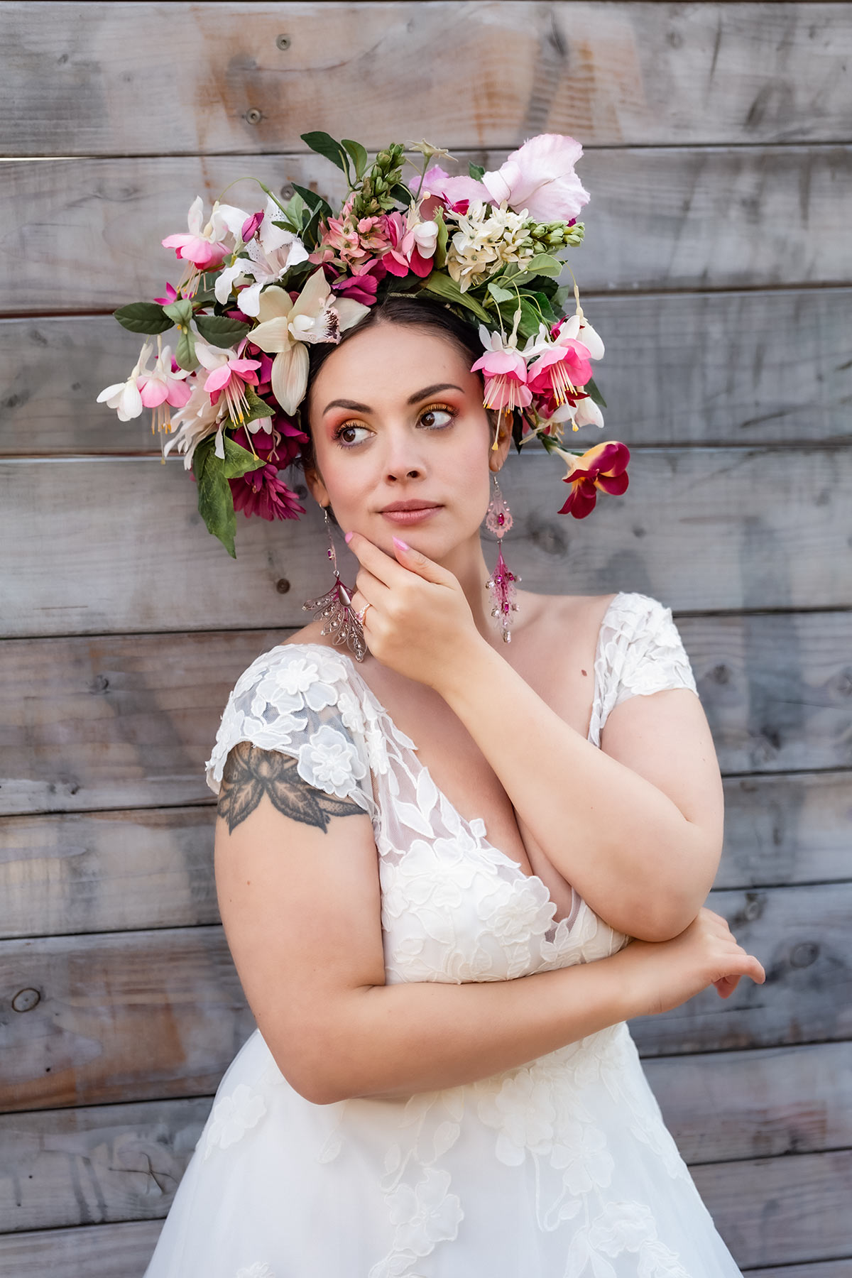 Bruden står lutad mot en grånande trävägg. På sig har hon en vit brudklänning och en stor blomsterkrona.