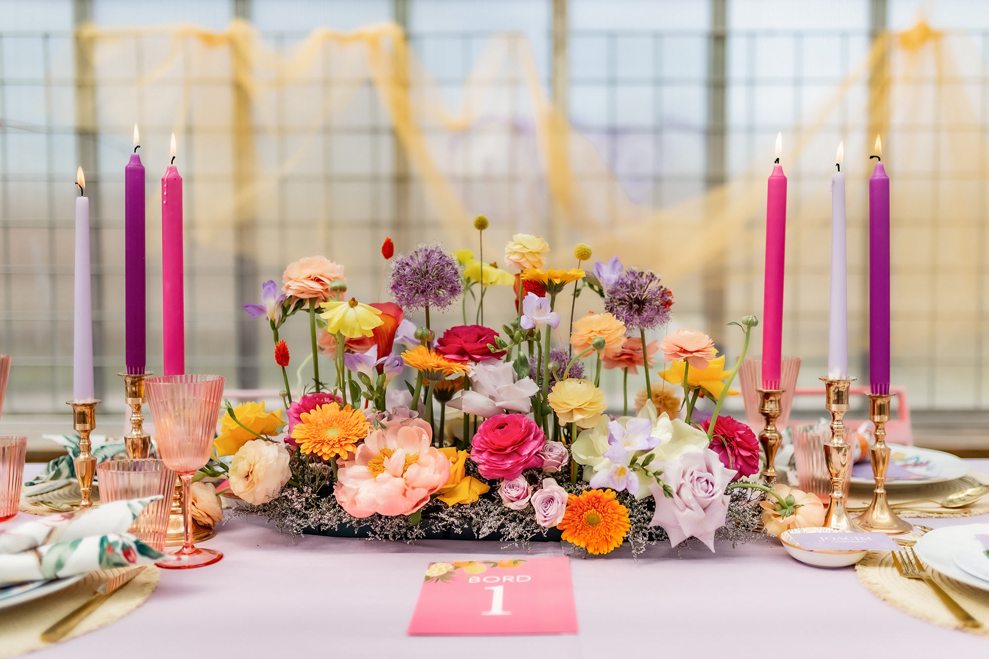 Ett vackert och färgglatt dukat bord med gigantiskt blomsterarrangemang och levande ljus.