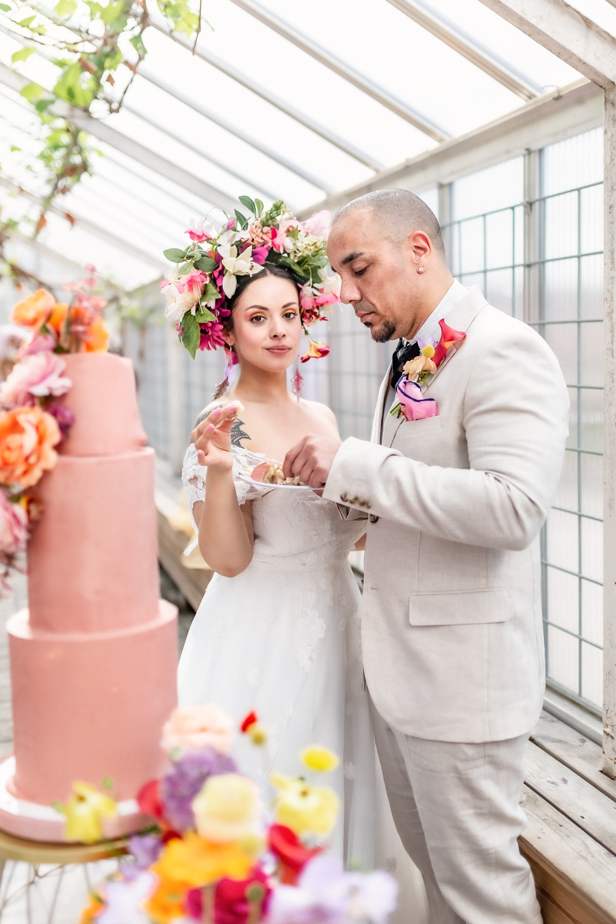 Bruden och brudgummen äter en tårtbit i ett växthus. Bruden tittar in i kameran.