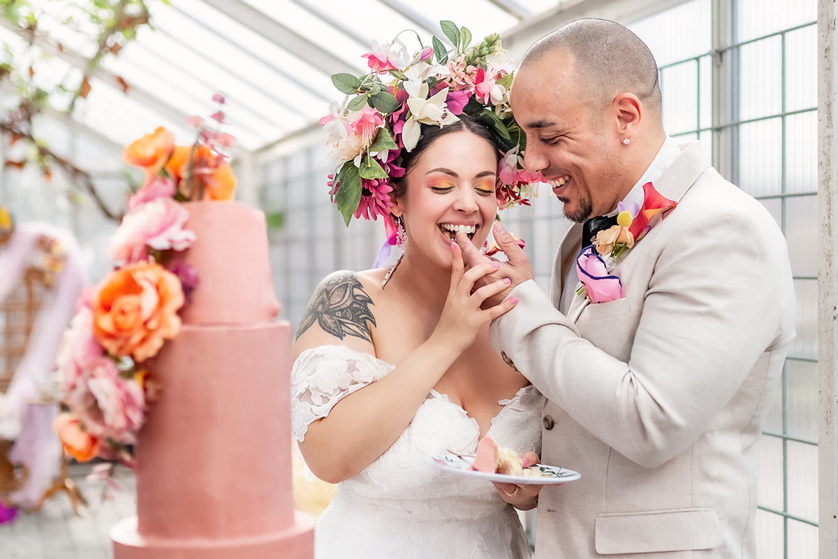 Bruden och  brudgrummen busar och skrattar medan de äter en tårtbit tillsammans.