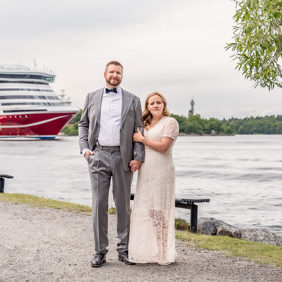 Brudpar står vid vattnet i Nacka. På andra sidan vattnet syns Kaknästornet, och på vattnet går en Viking Line-färja.