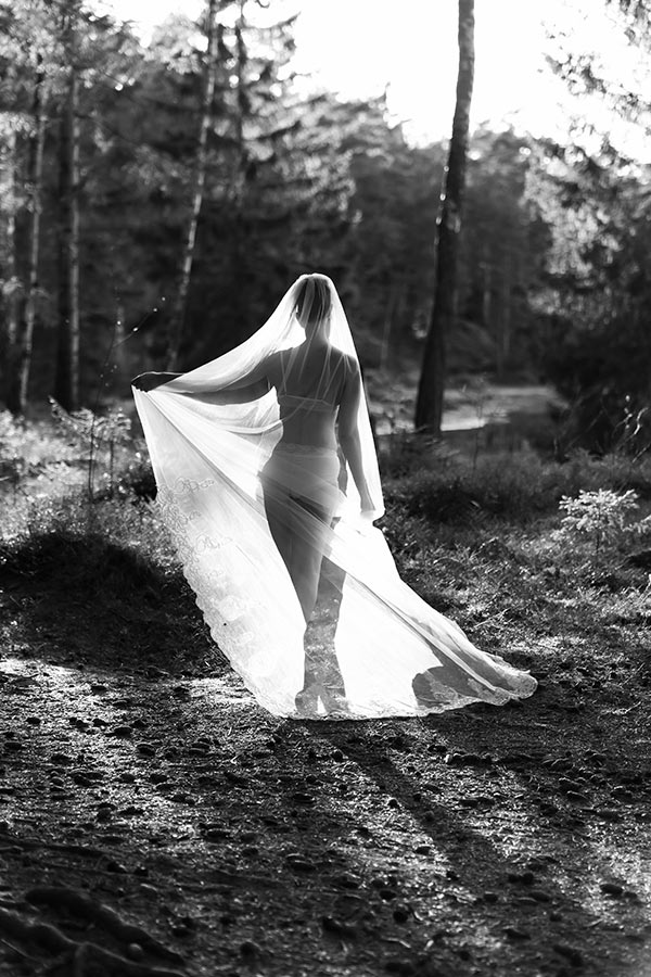 En svartvit bild på en kvinna i underkläder och slöja i skogen.