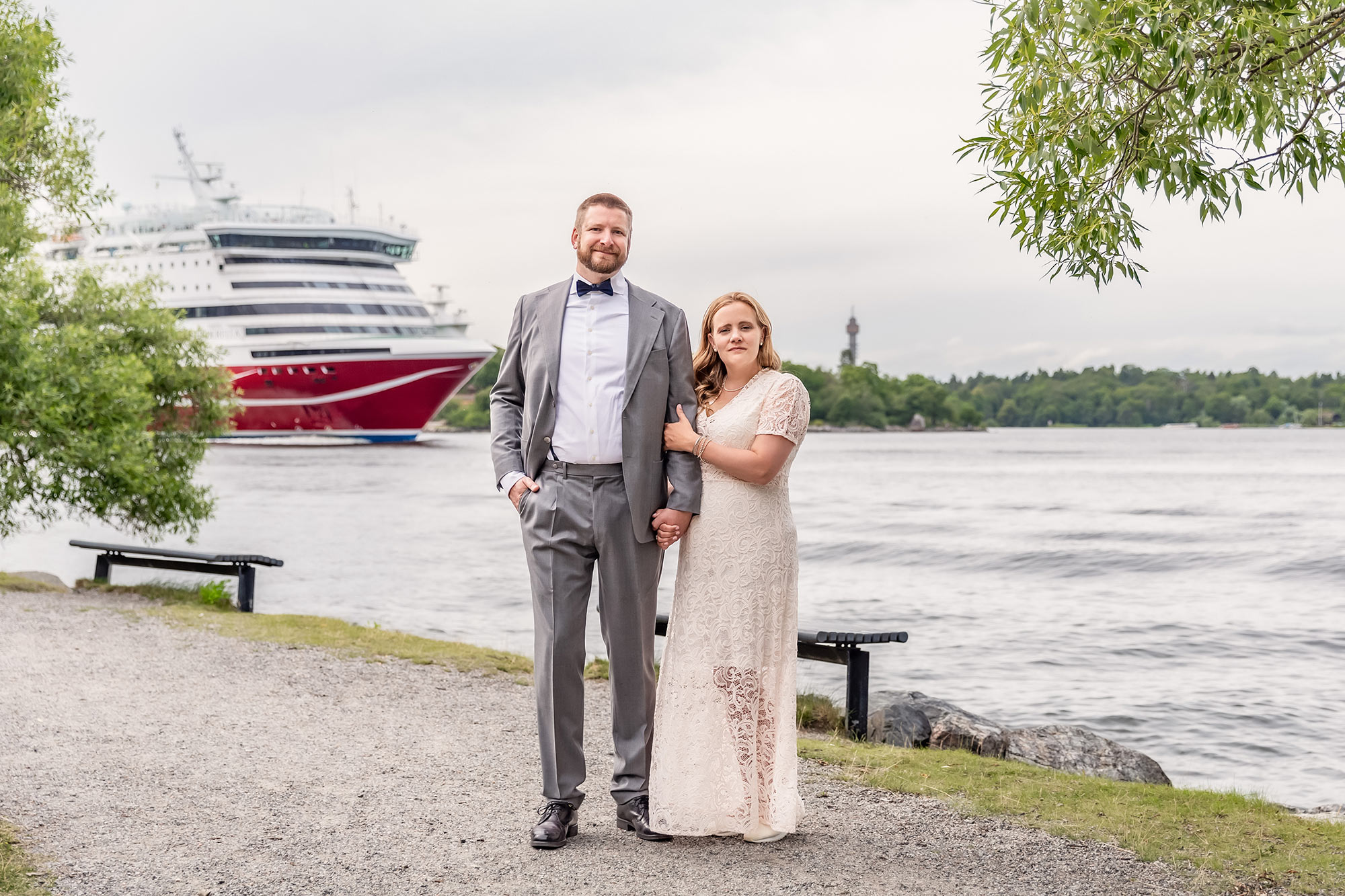 Brudpar står vid vattnet i Nacka. På andra sidan vattnet syns Kaknästornet, och på vattnet går en Viking Line-färja.