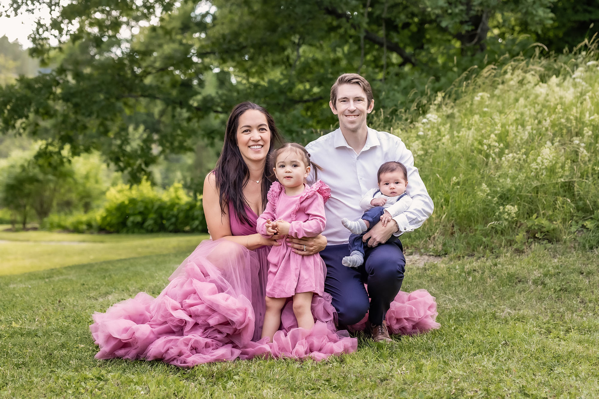 Familjefotografering bland grönskande gräs med familj med 2 små barn.