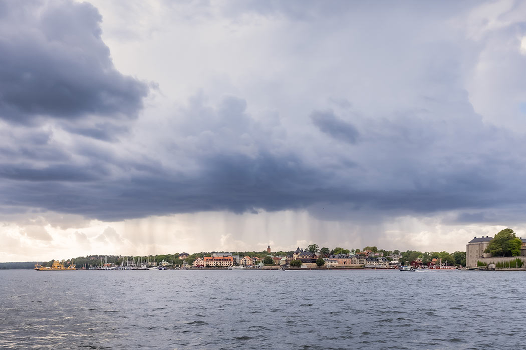 Vaxholm under mörka moln och regn. Bilden är tagen från en båt på väg från Badholmen till Vaxholm.