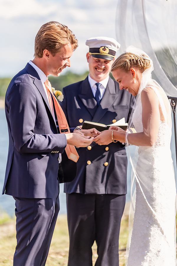 Brudpar utbyter ringar en solig sommardag vid vattnet.