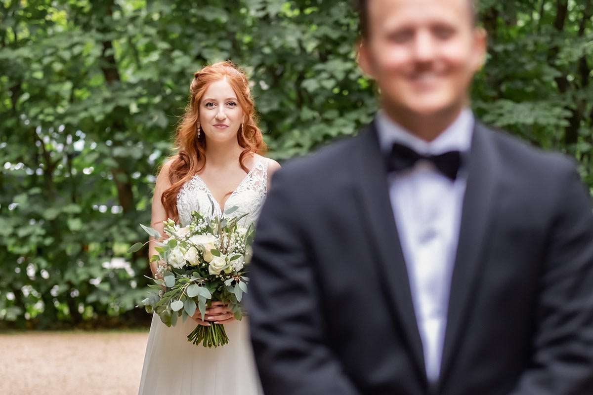 Fotografering av first look med fokus på bruden som kommer gående bakom brudgummen.