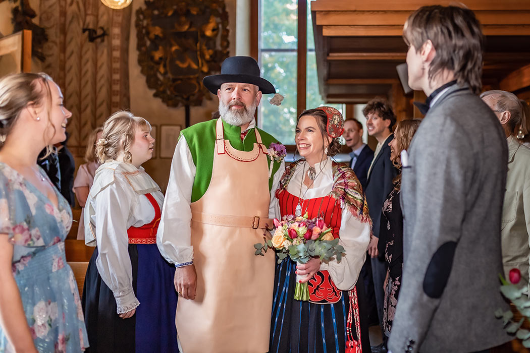 Ett brudpar som är klädda i folkdräkt går in i kyrkan. Kören står runt dem och sjunger medan de går.