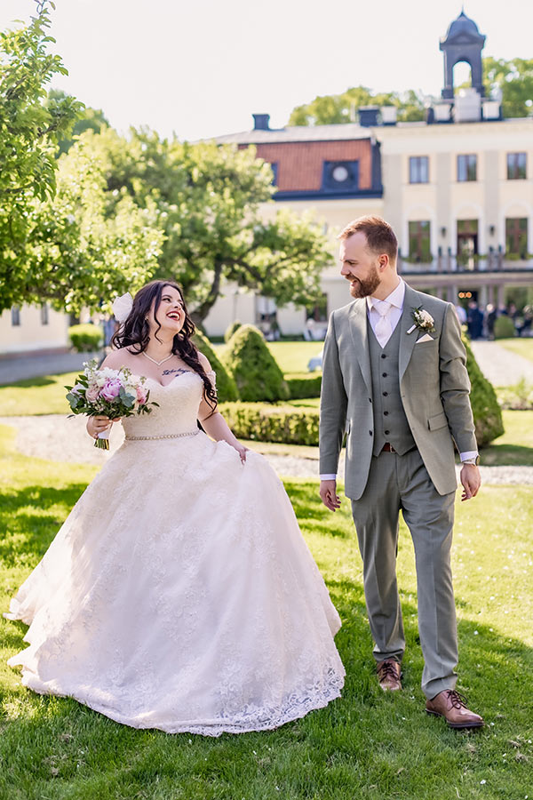 Bröllopsfotograf fotograferar bröllopspar när de går skrattandes bredvid varandra framför Södertuna Slott.